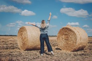 Eine übergewichtige Frau streckt an einem sonnigen Tag auf einem Weizenfeld voller Energie und Selbstbewusstsein ihre Arme in die Höhe.