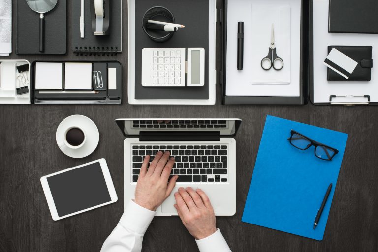 Die Unternehmenskommunikation, dargestellt durch verschiedene Bürobestandteile auf einem Schreibtisch wie Laptop, Tablet und Stift und Papier.