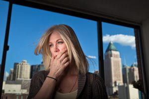 Eine junge Frau sitzt voller Angst im Büro, im Hintergrund ist ein Fenster mit Blick auf eine Großstadt zu sehen.